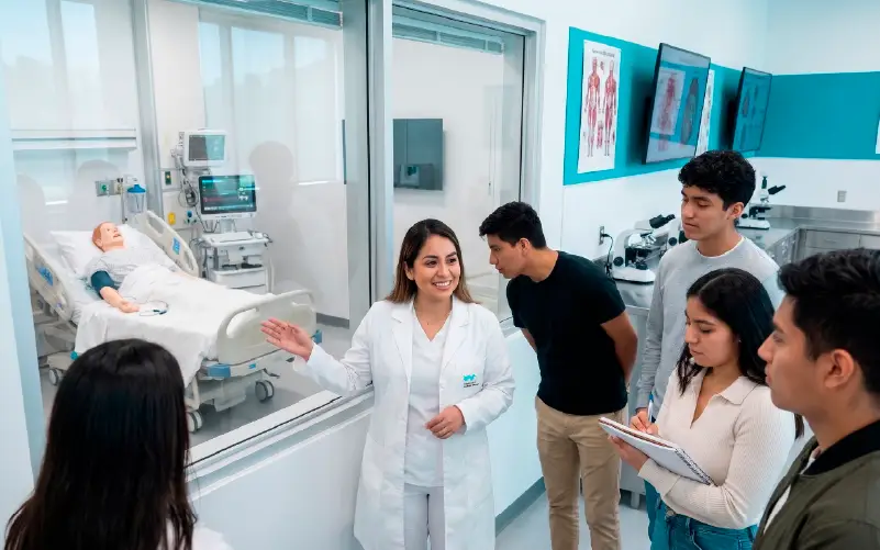 Guía mostrando una sala de simulación clínica a un grupo de estudiantes durante el recorrido